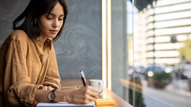A business woman sits in a cafe by the window and works, writes a reminder in her notebook